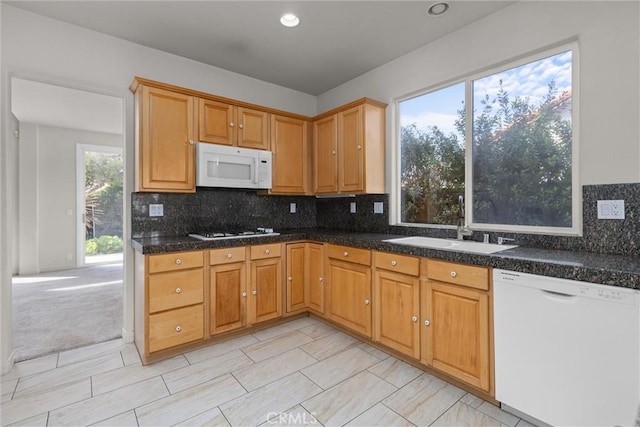 kitchen with a sink, backsplash, dark countertops, white appliances, and light colored carpet