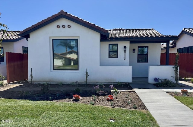 view of front of house featuring a tile roof, fence, a front lawn, and stucco siding