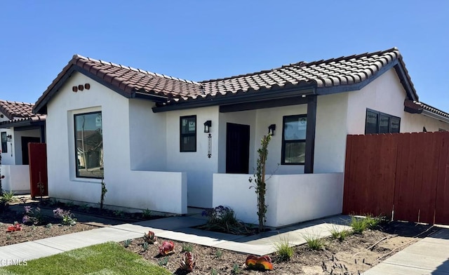 mediterranean / spanish-style home with a tile roof, fence, and stucco siding