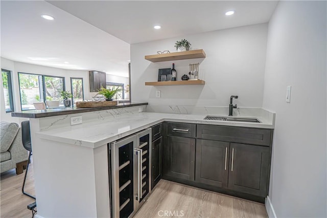 kitchen with light stone counters, a peninsula, light wood-style flooring, open shelves, and a sink