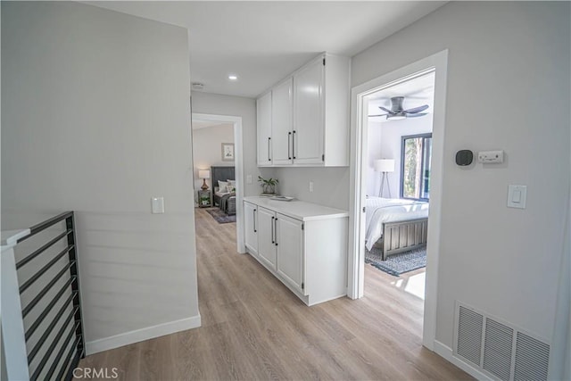 kitchen featuring baseboards, visible vents, light wood finished floors, light countertops, and white cabinetry