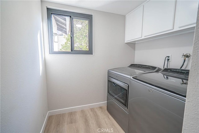 laundry area featuring washer and clothes dryer, cabinet space, light wood finished floors, and baseboards