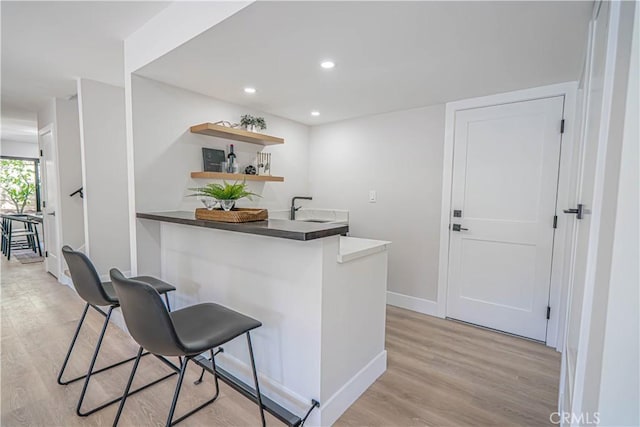 bar with light wood-style flooring, wet bar, baseboards, and a sink