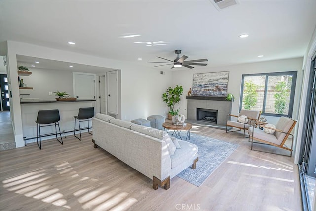 living area with light wood-type flooring, visible vents, a fireplace with raised hearth, recessed lighting, and ceiling fan