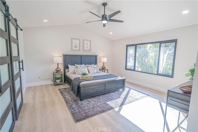 bedroom with a barn door, lofted ceiling, light wood-style floors, and baseboards