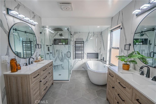 full bathroom featuring tile walls, two vanities, a marble finish shower, and a sink