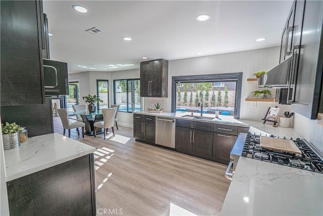 kitchen featuring visible vents, light wood-style flooring, a sink, light stone counters, and dishwasher