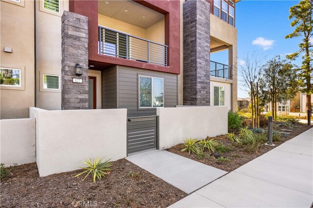 view of exterior entry with a gate, fence, stone siding, and a balcony