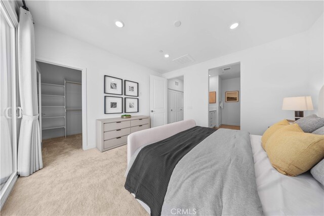bedroom with a closet, visible vents, recessed lighting, light carpet, and a walk in closet