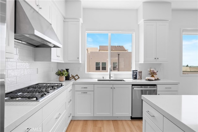 kitchen featuring stainless steel appliances, under cabinet range hood, a sink, backsplash, and light countertops