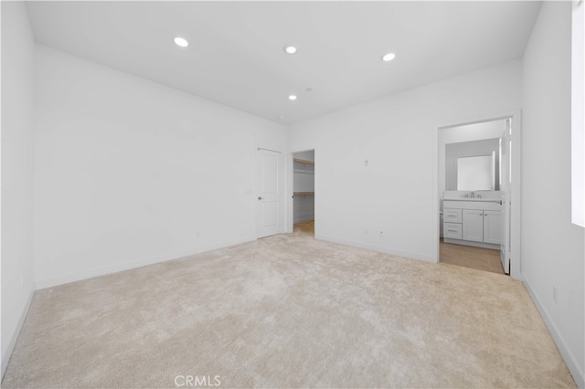 unfurnished bedroom with ensuite bathroom, recessed lighting, light carpet, a walk in closet, and baseboards