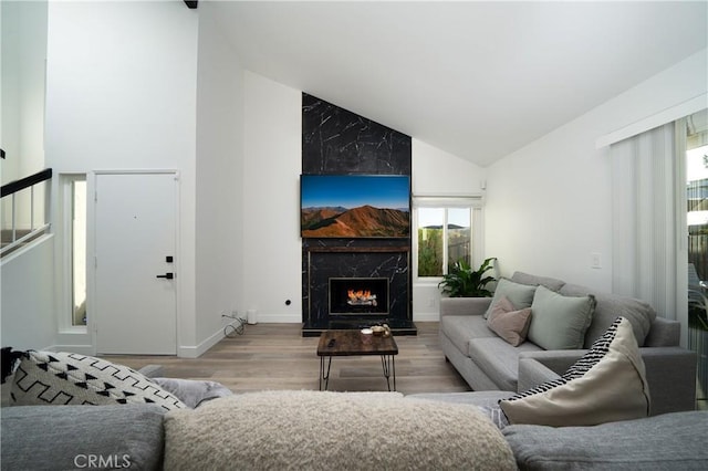 living area with baseboards, high vaulted ceiling, wood finished floors, and a high end fireplace