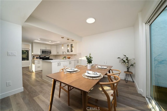 dining area with dark wood-style flooring, a raised ceiling, and baseboards