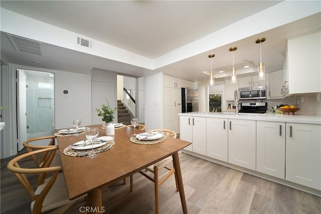 dining space featuring light wood finished floors, stairs, visible vents, and a raised ceiling