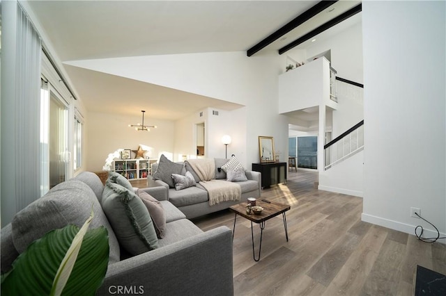 living room featuring wood finished floors, baseboards, stairs, beam ceiling, and an inviting chandelier