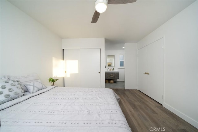 bedroom featuring baseboards, connected bathroom, ceiling fan, wood finished floors, and two closets