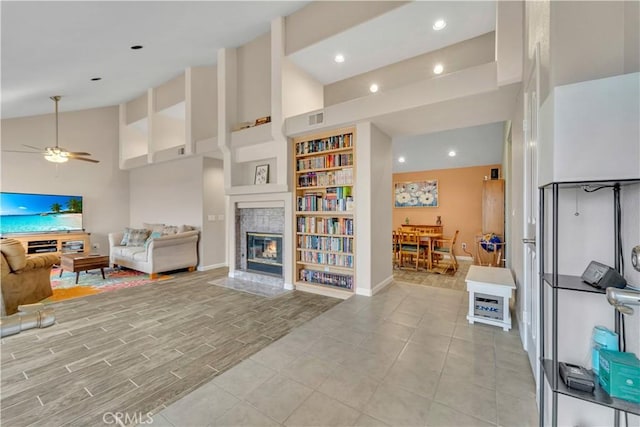 living area with ceiling fan, high vaulted ceiling, a fireplace, visible vents, and baseboards