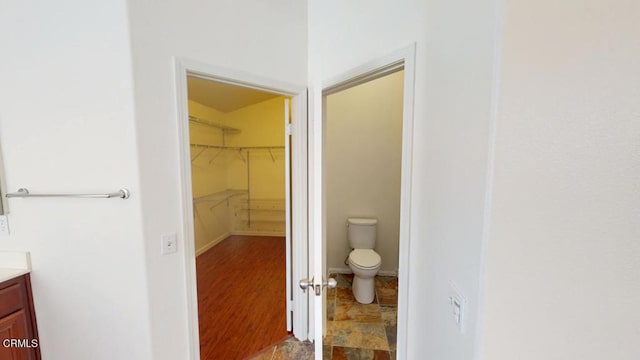 bathroom with baseboards, toilet, a walk in closet, and vanity