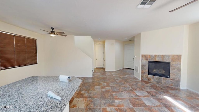 unfurnished living room featuring a ceiling fan, a tile fireplace, baseboards, and visible vents