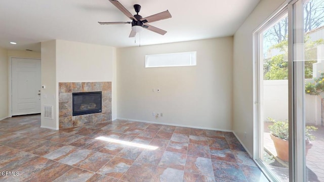 unfurnished living room featuring stone finish floor, baseboards, ceiling fan, a tiled fireplace, and visible vents