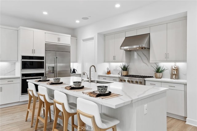 kitchen featuring a sink, stove, built in fridge, wall oven, and exhaust hood