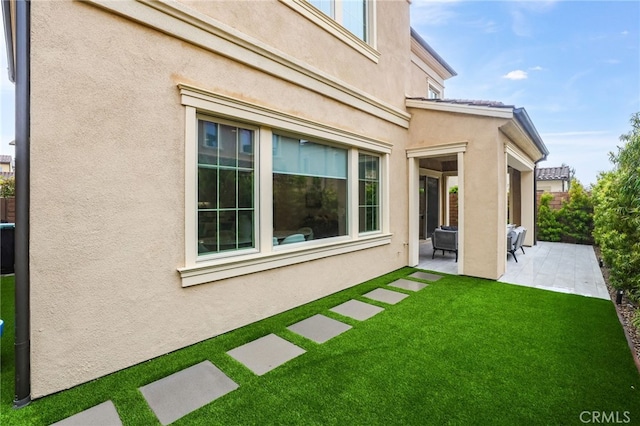 rear view of property featuring a patio area, stucco siding, a yard, and fence