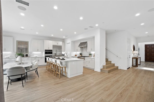 kitchen featuring visible vents, wall chimney range hood, an island with sink, stainless steel appliances, and a sink