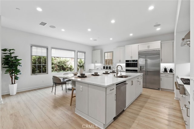 kitchen with light wood-style flooring, recessed lighting, a kitchen island with sink, stainless steel appliances, and white cabinetry