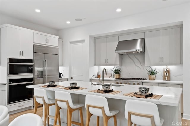 kitchen with tasteful backsplash, light countertops, a kitchen bar, range hood, and a sink