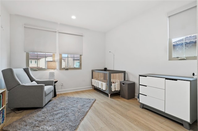 bedroom featuring a crib, recessed lighting, baseboards, and light wood finished floors