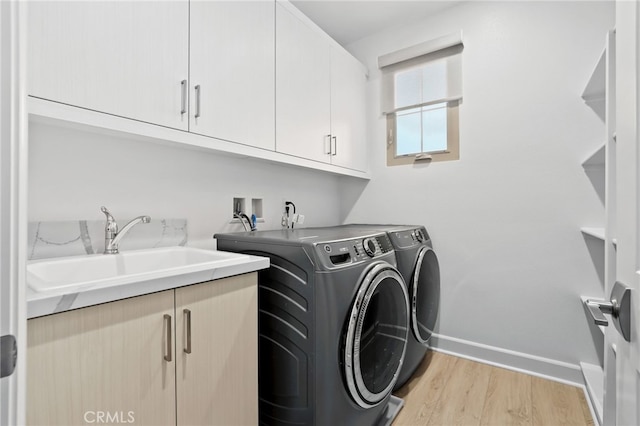 laundry area with baseboards, light wood finished floors, separate washer and dryer, cabinet space, and a sink