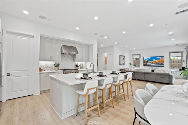 kitchen with range hood, visible vents, a center island with sink, light wood-style flooring, and a kitchen breakfast bar