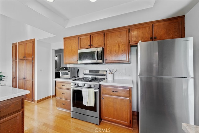 kitchen featuring stainless steel appliances, light wood-style flooring, brown cabinetry, and light countertops