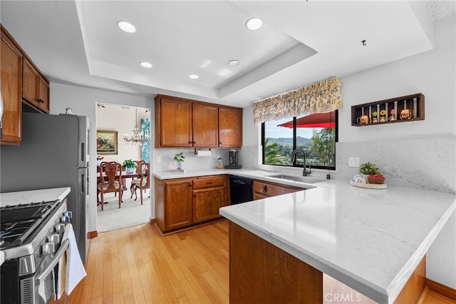 kitchen featuring a sink, a tray ceiling, a peninsula, brown cabinetry, and stainless steel gas range