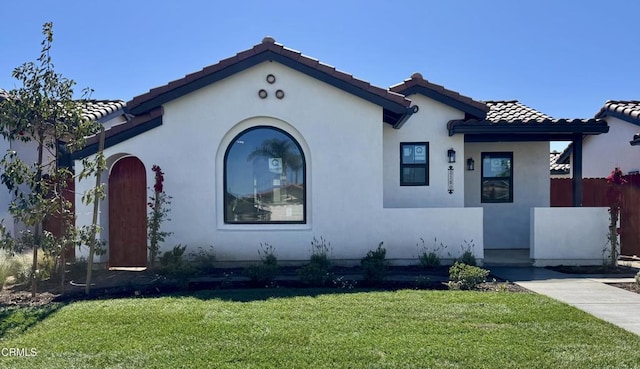 mediterranean / spanish home with a front yard, fence, a tiled roof, and stucco siding