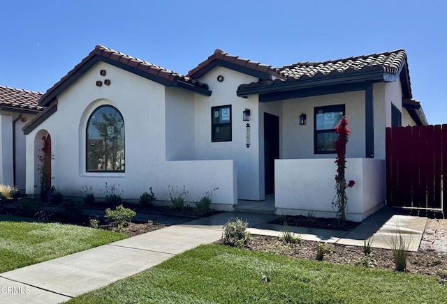 mediterranean / spanish-style home featuring a tile roof, fence, a front lawn, and stucco siding