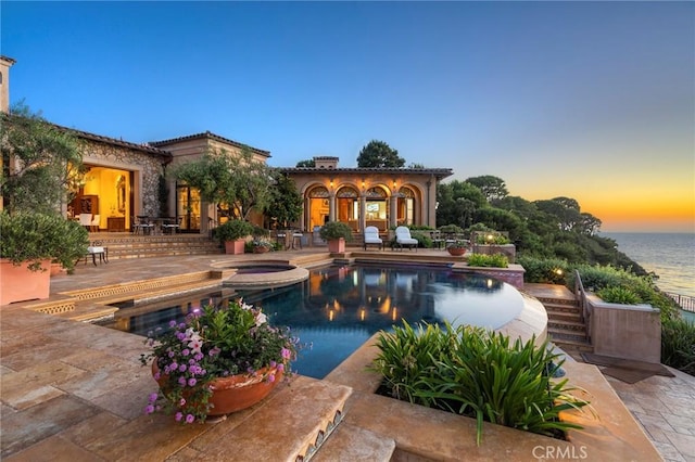 pool at dusk featuring a patio area and a pool with connected hot tub