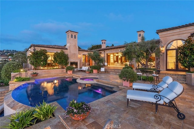 view of swimming pool featuring a pool with connected hot tub, a warm lit fireplace, and a patio