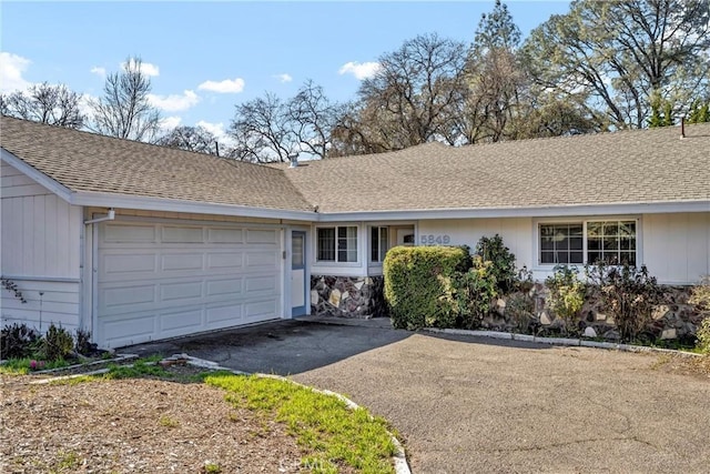 ranch-style home featuring an attached garage, aphalt driveway, and a shingled roof