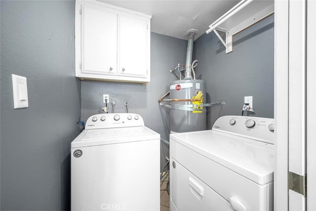 clothes washing area featuring water heater, washer and clothes dryer, and cabinet space