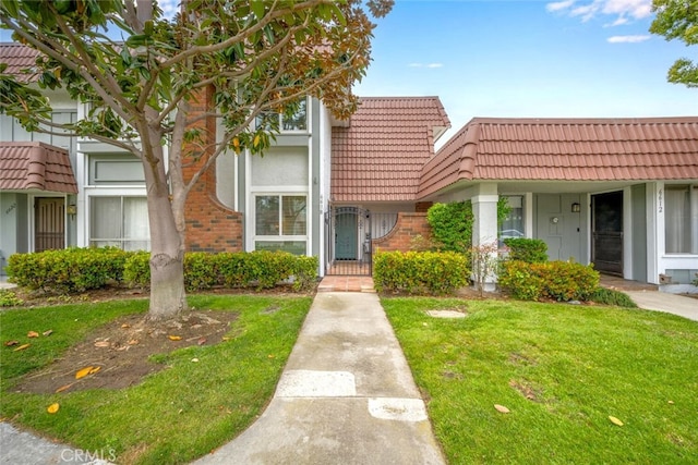 view of front of home featuring a front yard, a tiled roof, and brick siding