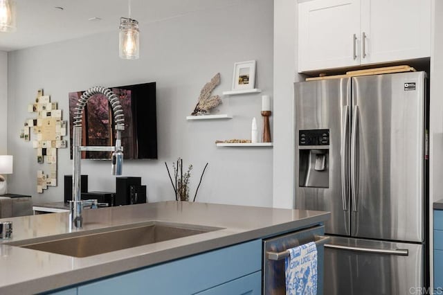 kitchen featuring stainless steel appliances, a sink, white cabinetry, light countertops, and decorative light fixtures