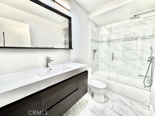 full bath with enclosed tub / shower combo, marble finish floor, toilet, and vanity