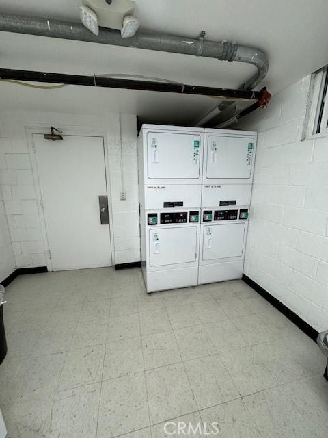 shared laundry area with concrete block wall, light floors, and stacked washer and clothes dryer