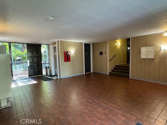 interior space with stairs, a textured ceiling, wood walls, and expansive windows