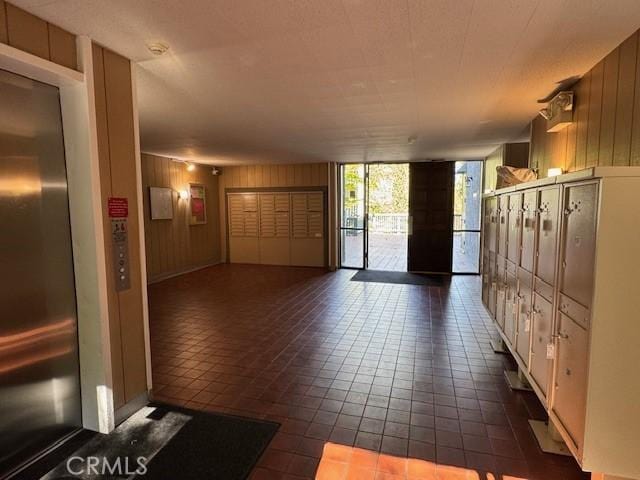 interior space featuring wooden walls, mail area, elevator, expansive windows, and dark tile patterned floors