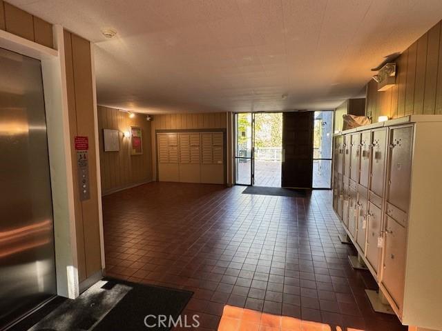 3601 W Hidden Ln Unit 309, Rolling Hills Estates, CA 90274 - foyer entrance with floor to ceiling windows, wood walls, dark tile patterned flooring, mail area, and elevator