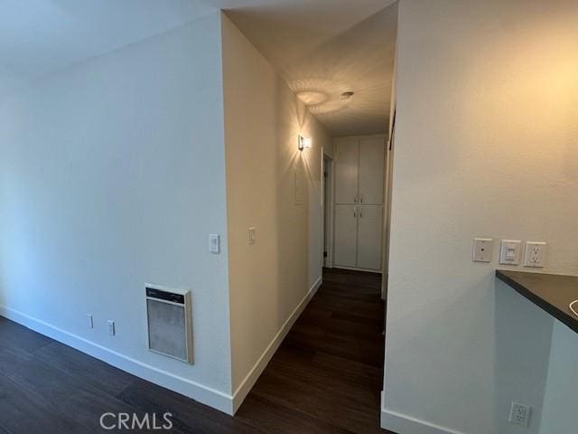 corridor featuring dark wood finished floors, heating unit, and baseboards