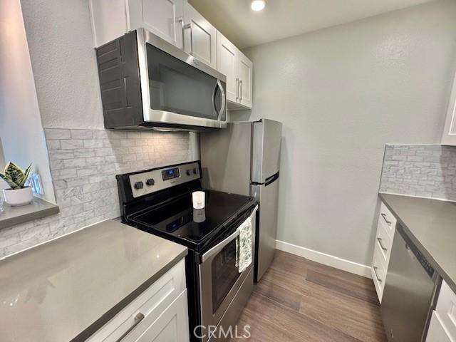 3601 W Hidden Ln Unit 309, Rolling Hills Estates, CA 90274 - kitchen with appliances with stainless steel finishes, backsplash, dark wood-style flooring, white cabinets, and baseboards