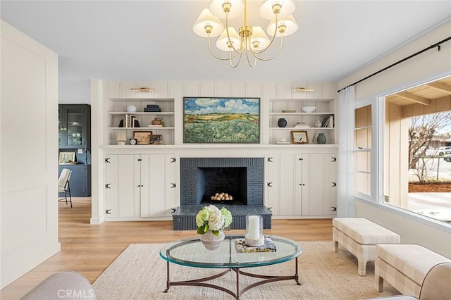 living area featuring built in features, light wood-type flooring, a brick fireplace, and a notable chandelier